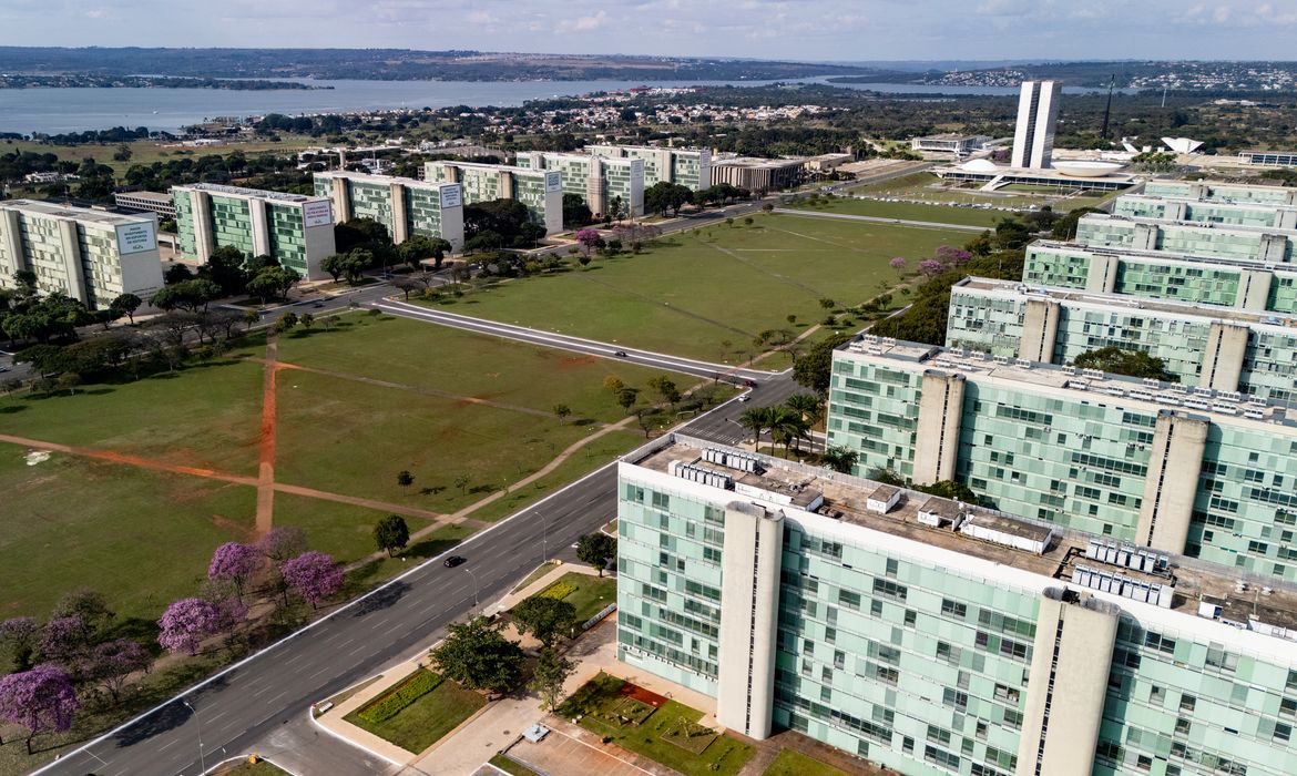 22/06/2026 - Brasília - A floração dos ipês-roxos transforma a paisagem de Brasília em um espetáculo de cores que dura apenas algumas semanas, mas deixa marcas na memória durante todo o ano. Considerada uma das árvores mais simbólicas do Cerrado brasileiro, o ipê anuncia a chegada da estação seca justamente quando perde suas folhas e exibe flores em tons vibrantes que contrastam com o céu azul da Esplanada dos Ministérios.  Em meio às linhas retas, ao concreto aparente e aos tons cinza característicos da arquitetura modernista idealizada por Oscar Niemeyer, os ipês surgem como protagonistas da paisagem urbana. A explosão de flores roxas quebra a monotonia das formas e colore avenidas, parques e áreas residenciais, criando uma das cenas mais marcantes da capital federal. Breve e intensa, a floração dos ipês lembra que alguns dos mais belos espetáculos da natureza são também os mais passageiros. Foto: Rafa Neddermeyer/Agência Brasil